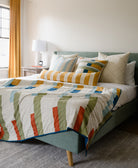 multi-colored stripe patchwork quilt draped over end of colorful upholstered bed