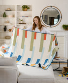 woman unfolding stamp patchwork quilt in all white living room