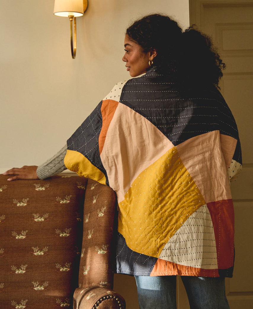 woman wearing abstract colorful cocoon quilted jacket standing next to a brown upholstered chair