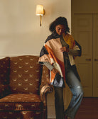 woman wearing colorful quilted jacket with hand-stitched embroidery standing next to vintage brown upholstered chair
