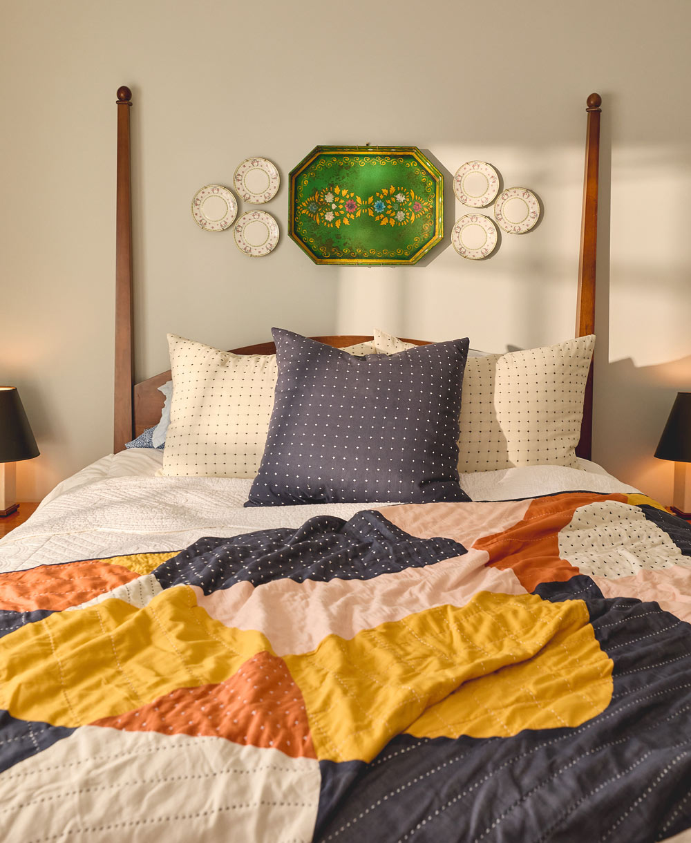 Bed with colorful quilt and pillows, wooden headboard, and decorative wall art
