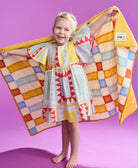 Young girl holding tile quilt up behind her standing on a pink background