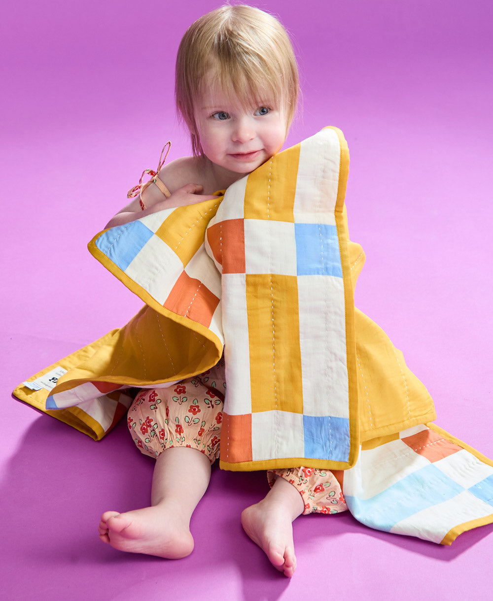 Toddler wrapped in tile baby quilt sitting on the ground