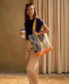 Woman holding a colorful tote bag and a coffee cup against a beige curtain background