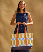 woman holding checkered canvas tote bag in blue, olive green, sky blue and orange while wearing blue dress