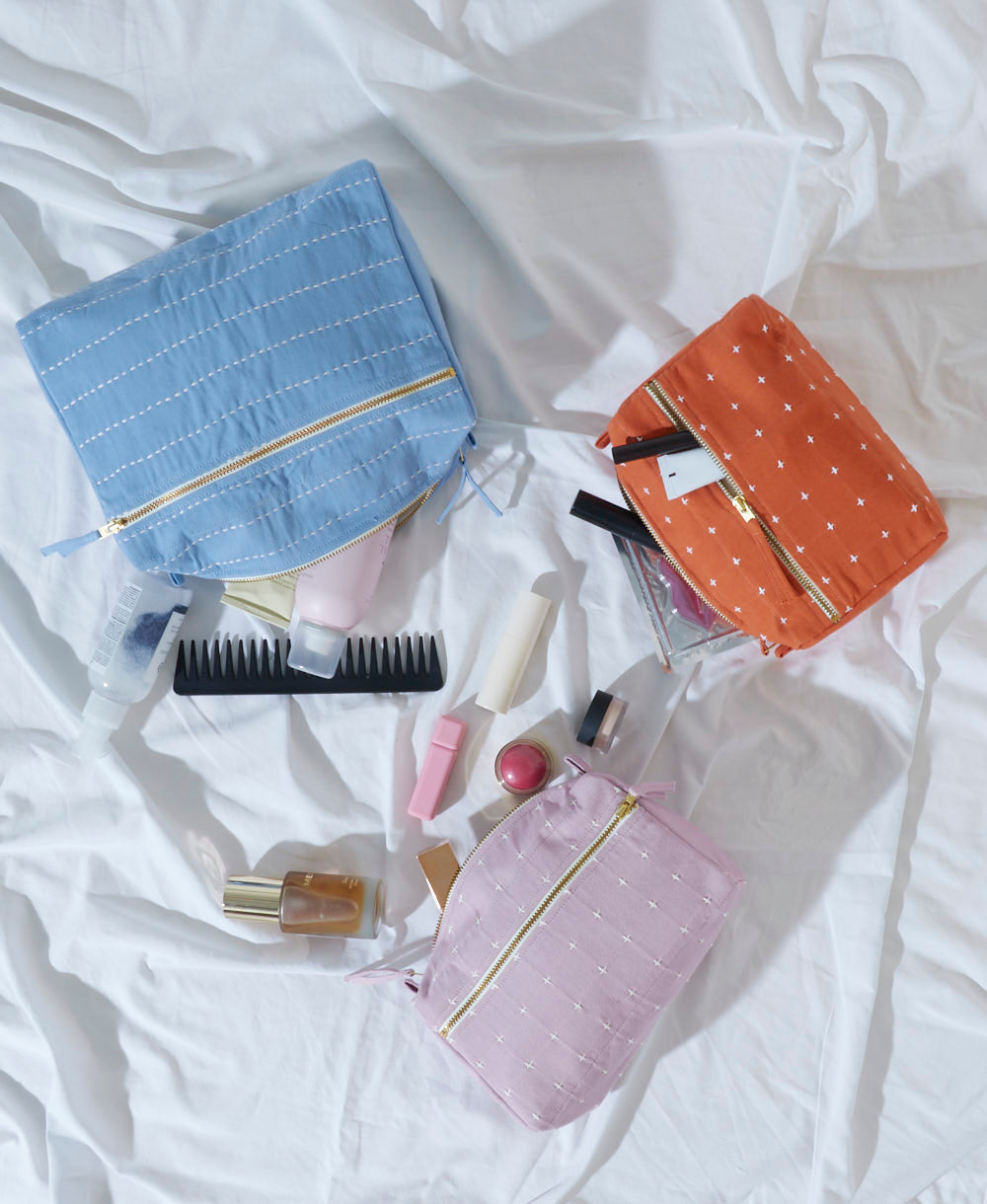 Set of colorful pouches with cosmetic items on a white fabric background