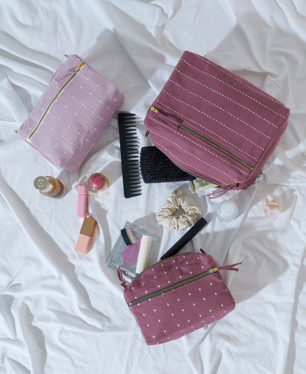 Pink toiletry bags with travel-sized products on a white bedspread