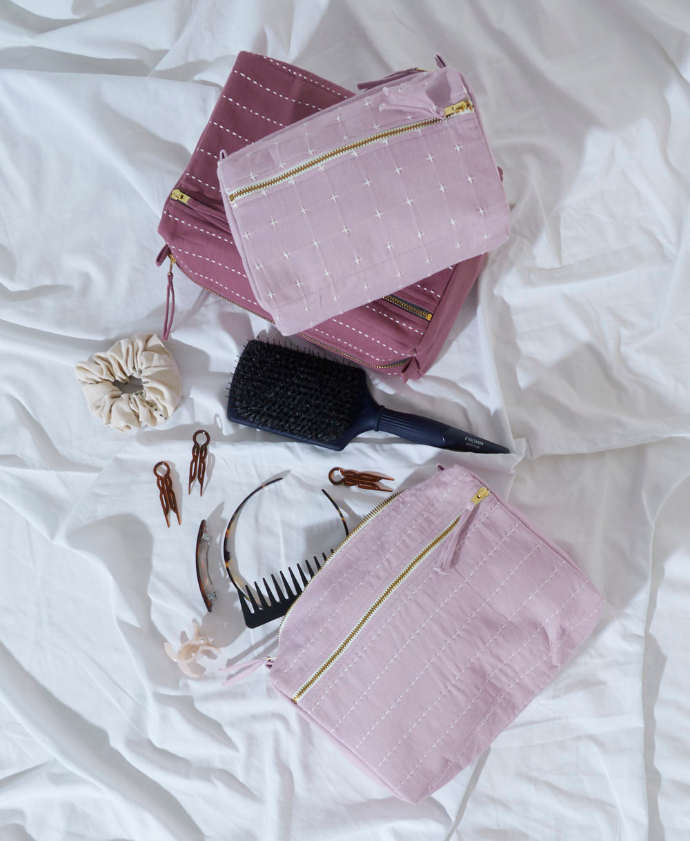 Pink toiletry bags with gold zippers on a white surface with hairbrush and accessories.