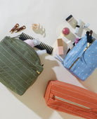 Three cosmetic bags with various travel-sized products on a light background