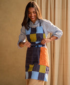 Woman wearing a colorful patchwork bib apron against a beige curtain background