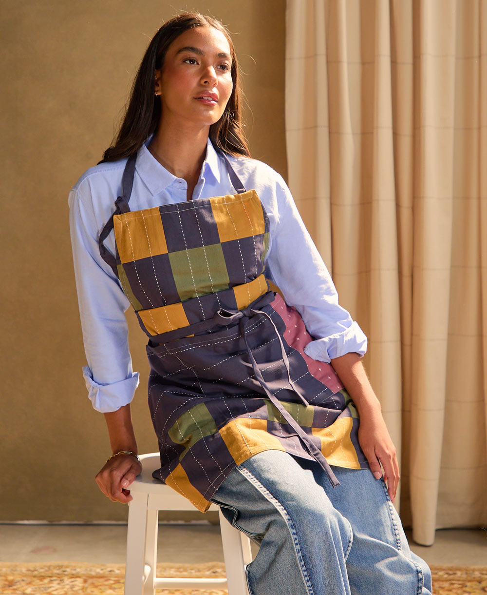 Woman wearing a colorful checkered bib apron sitting on a stool.