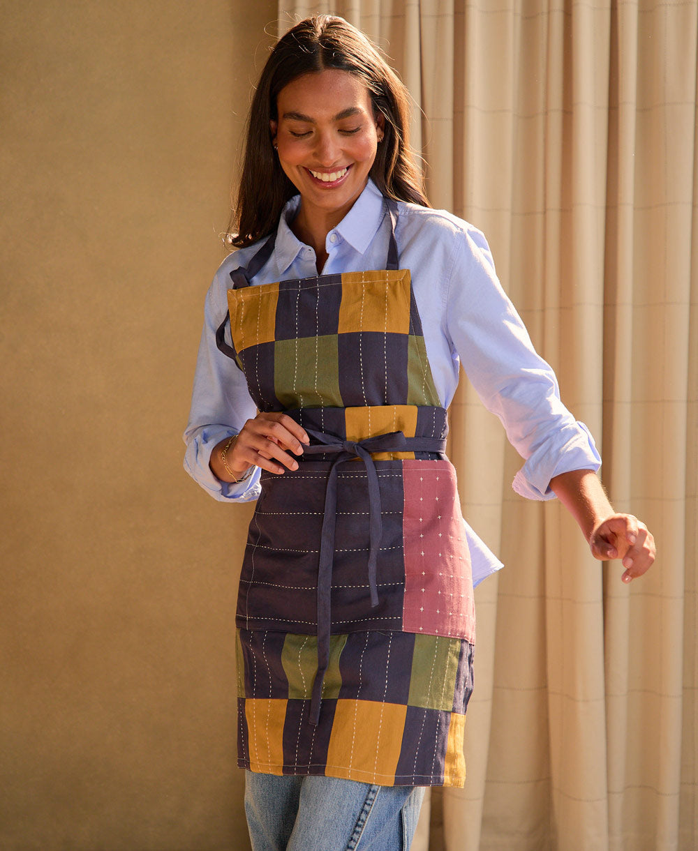 Woman wearing a colorful patchwork apron against a beige curtain background