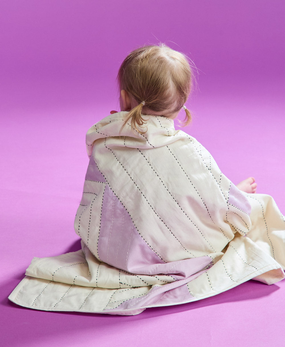 back of toddler sitting on purple backdrop with triangle quilt wrapped around her