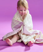 toddler sitting with the triangle baby quilt wrapped around her on a purple backdrop
