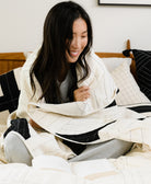 woman wrapped in black and white triangle patchwork quilt on all white bed