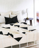 black and white triangle patchwork quilt draped over all white modern bed with matching monochromatic pillows