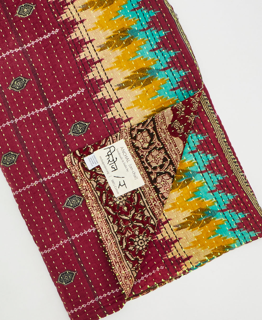 Kantha quilt throw with a tag featuring the hand-stitched signature of the maker