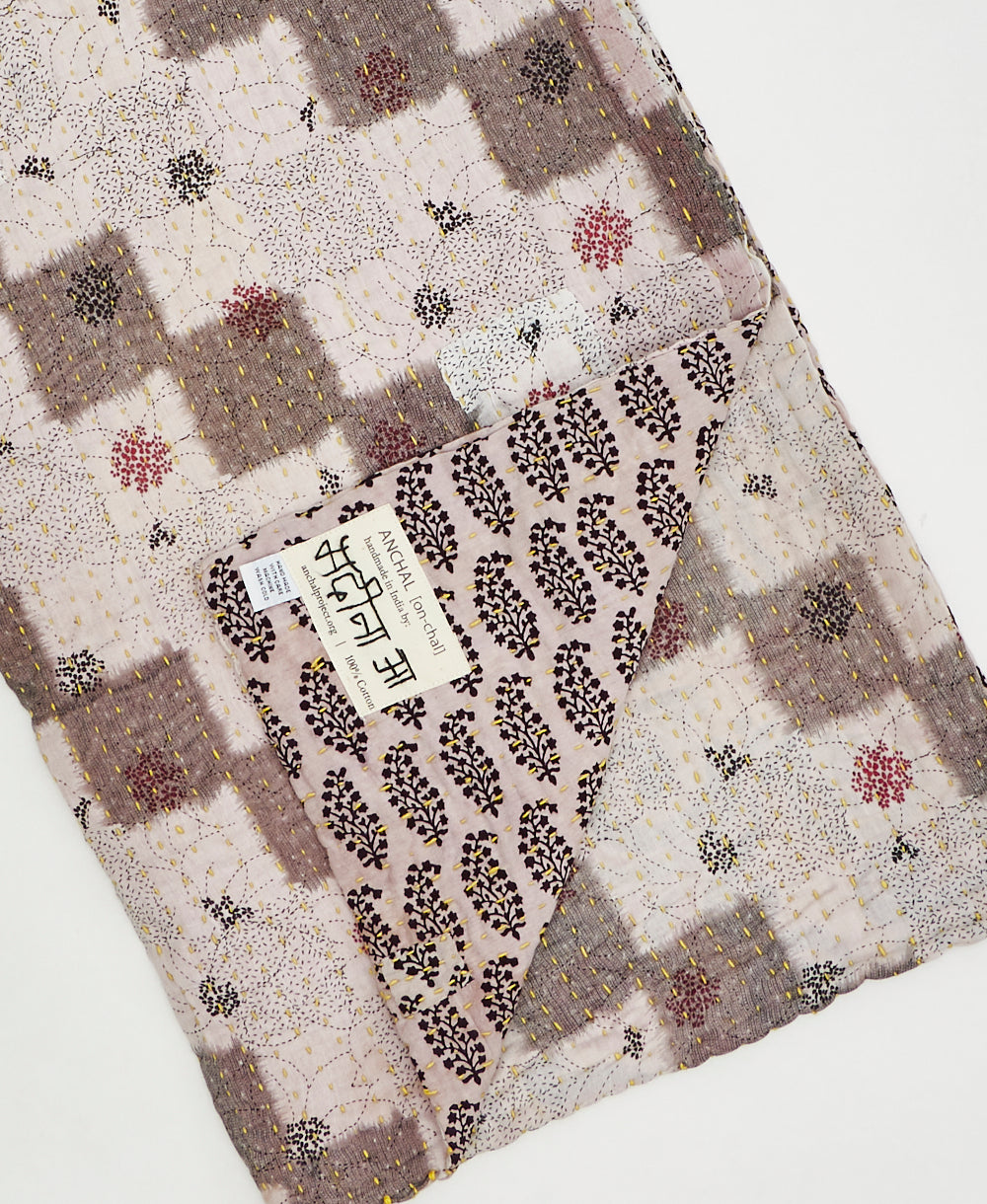 Kantha quilt throw with a tag featuring the hand-stitched signature of the maker