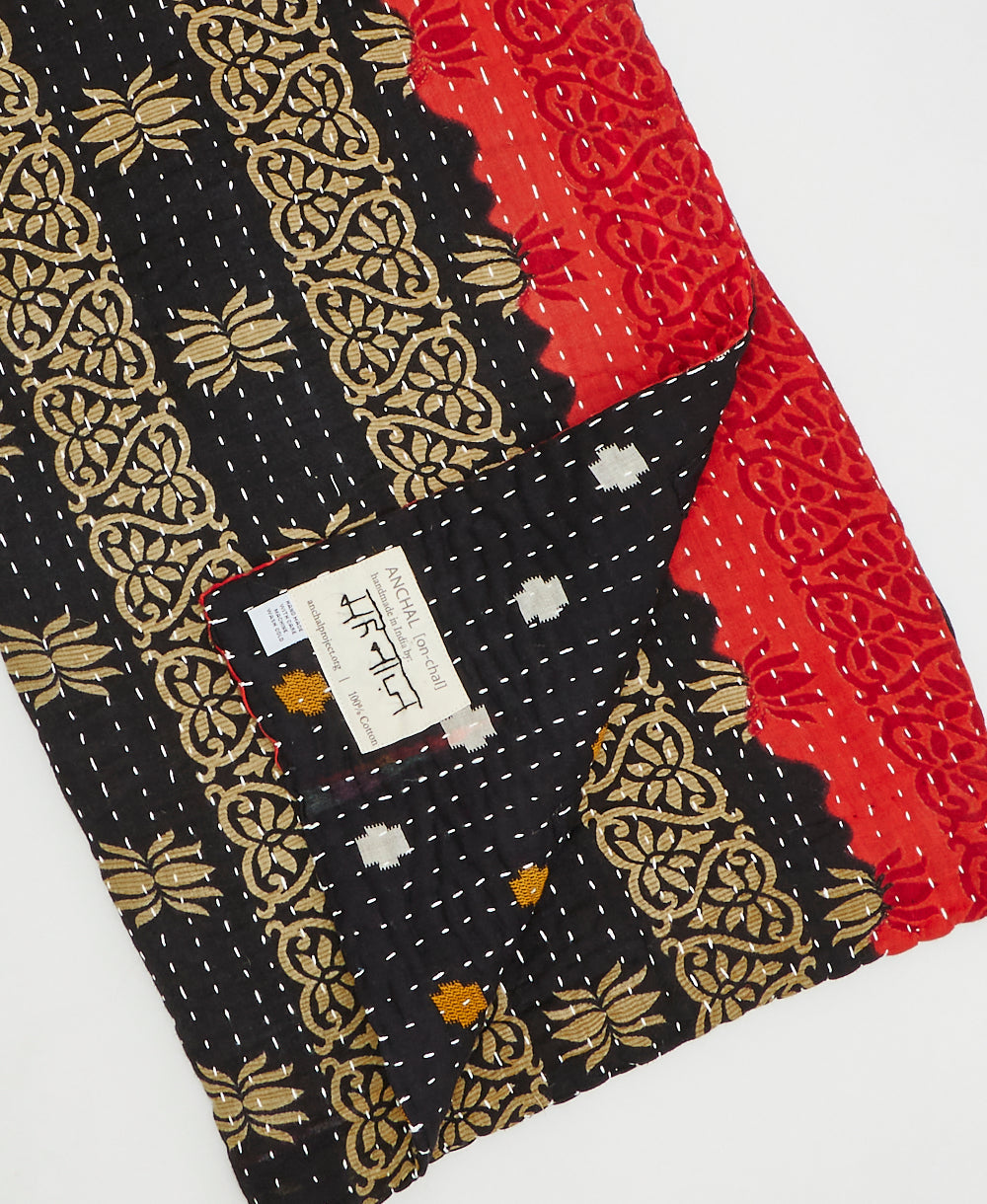 Kantha quilt throw with a tag featuring the hand-stitched signature of the maker