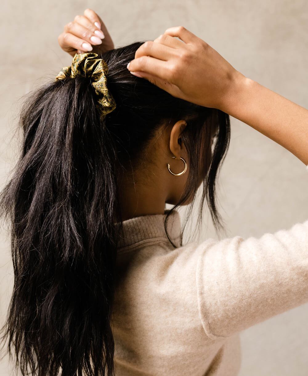 woman with dark wavy hair wearing a high ponytail with a vintage silk scrunchie in olive green