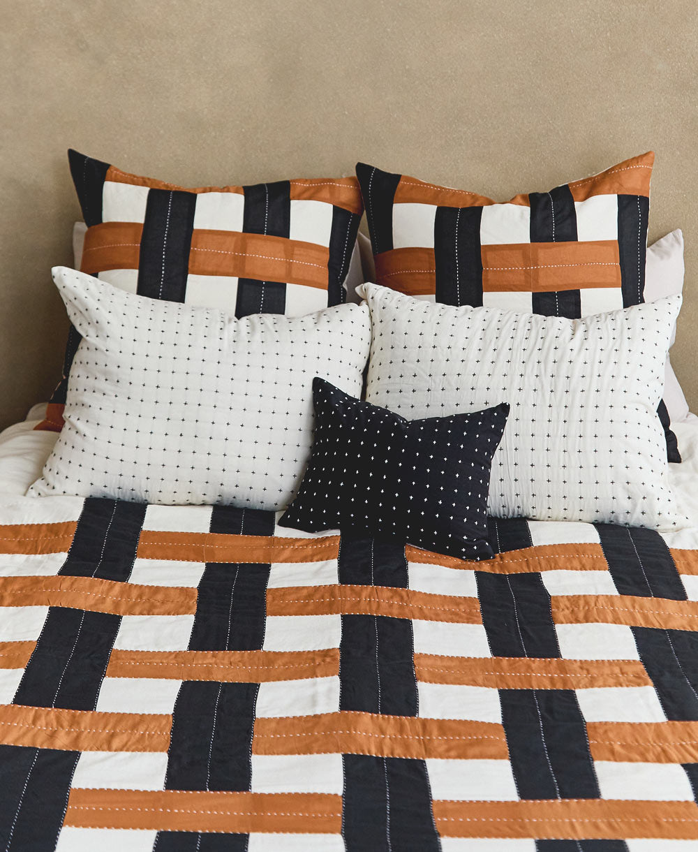 camel, black and white intersecting patchwork quilt on queen bed with matching plaid euro shams and embroidered pillows