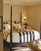 Bedroom with a four-poster bed featuring striped bedding, pillows, and a lamp on the wall