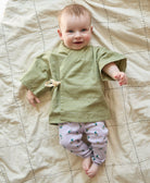 baby girl wearing sage green wrap baby top with drop shoulder sleeves and tie front closure