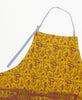 apron hadmade in Ajmer by woman artisans featurng brown and green swirling floral patterns on a yellow bakground with slate blue adjustable straps