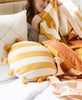 Anchal Project mustard stripe cabana tassel pillow and offset quilted throw blanket on a white bed