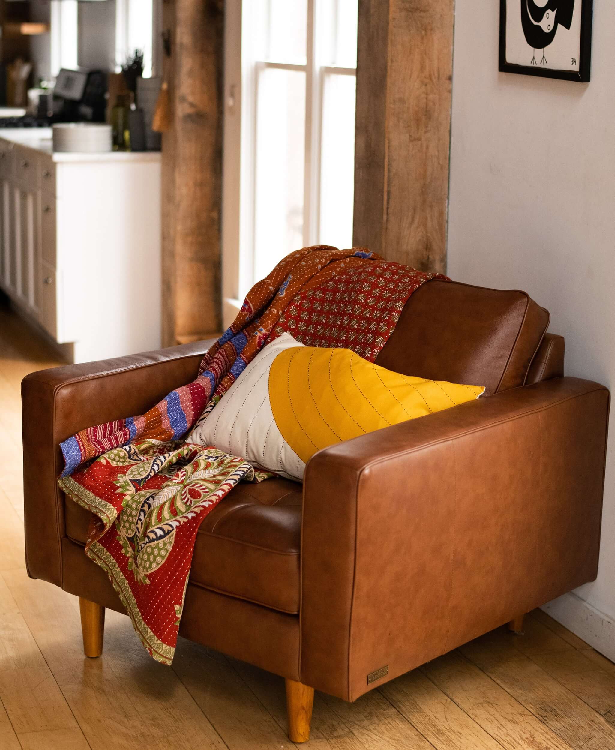 mustard yellow lumbar pillow with curve design in chestnut brown modern leather armchair accented with red kantha quilt