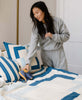 Woman placing stuffed elephant on bed with white organic cotton cotton quilt and pillow featuring dark and light blue geometric designs