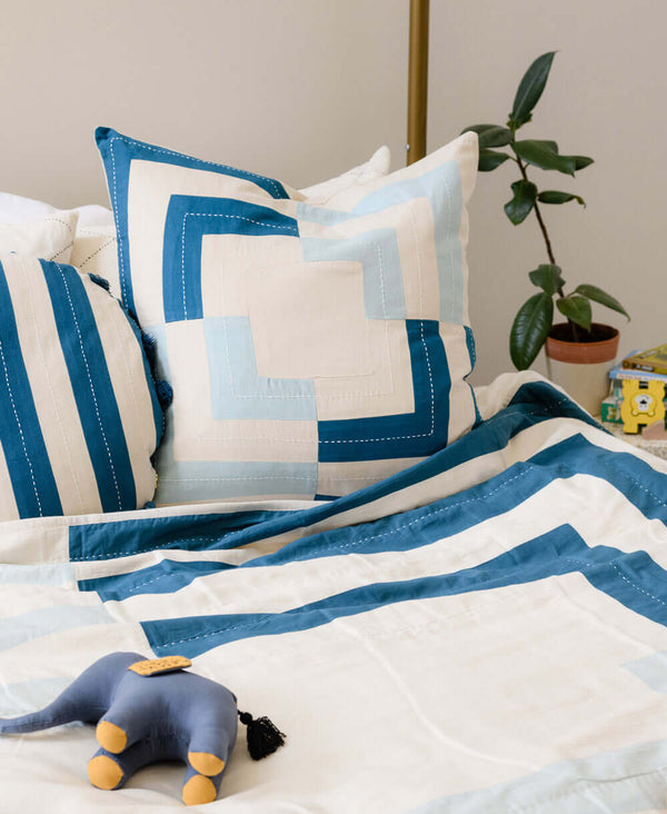 fracture throw pillow with patchwork square design on blue and white bed