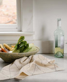 natural ivory tea towel with hand-embroidered gris stitching sitting on counter top