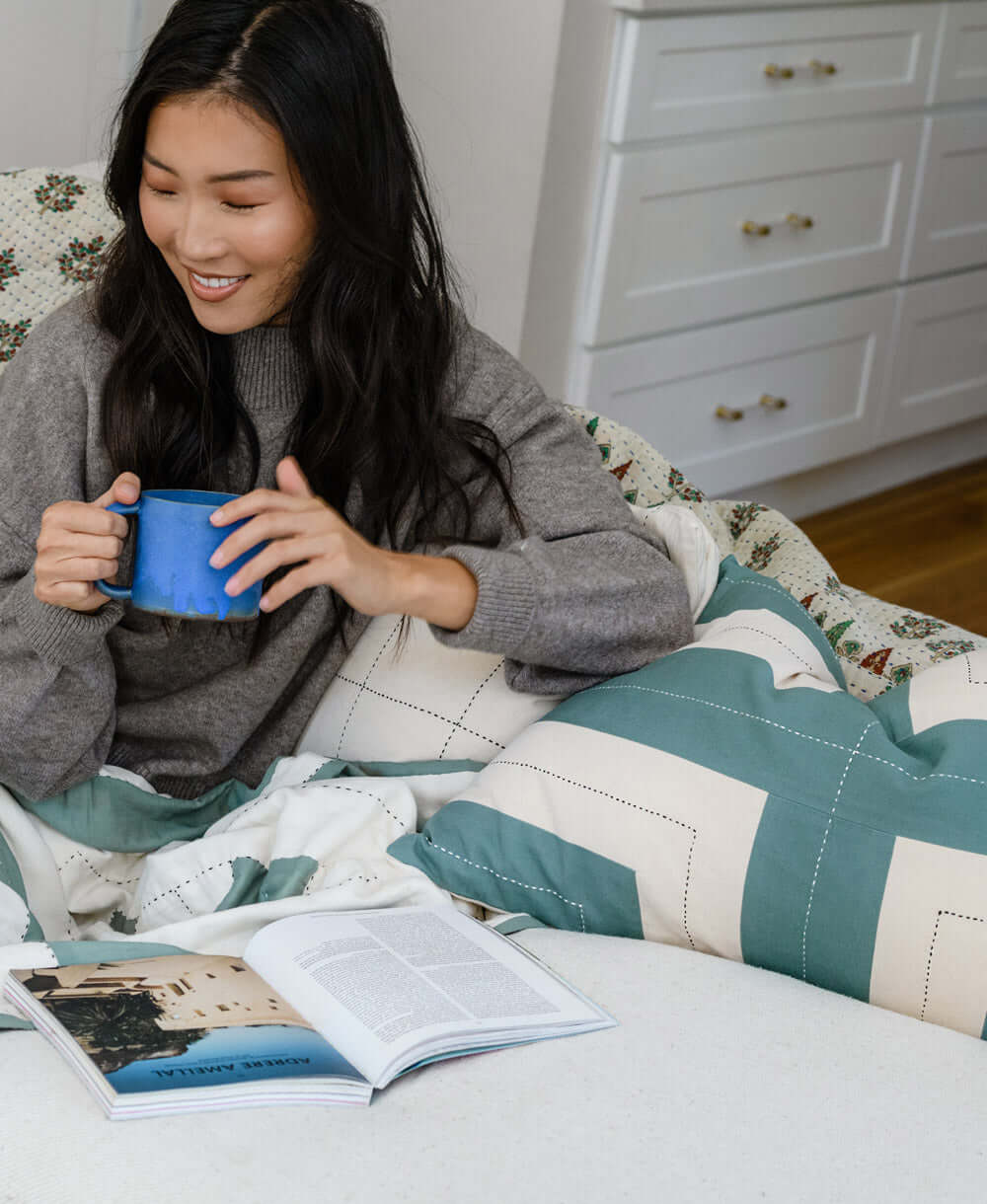 woman enjoying a cup of coffee on white sofa with embroidered throw pillows