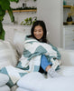 woman draped in buttery soft modern quilt in beige sofa by Anchal Project