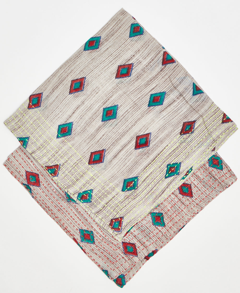 two beige cototn bandanas with read and teal diamonds stacked on top of each other to sow the difference in thread color. one has neon yellow kantha stitching along its edges while the other has red kantha stitching 