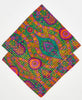 two teal, purple, orange, and yellow paisley patterned bandanas stacked on top of each other to show the different thread colors. one has white kantha stitching along its edges while the other has pink