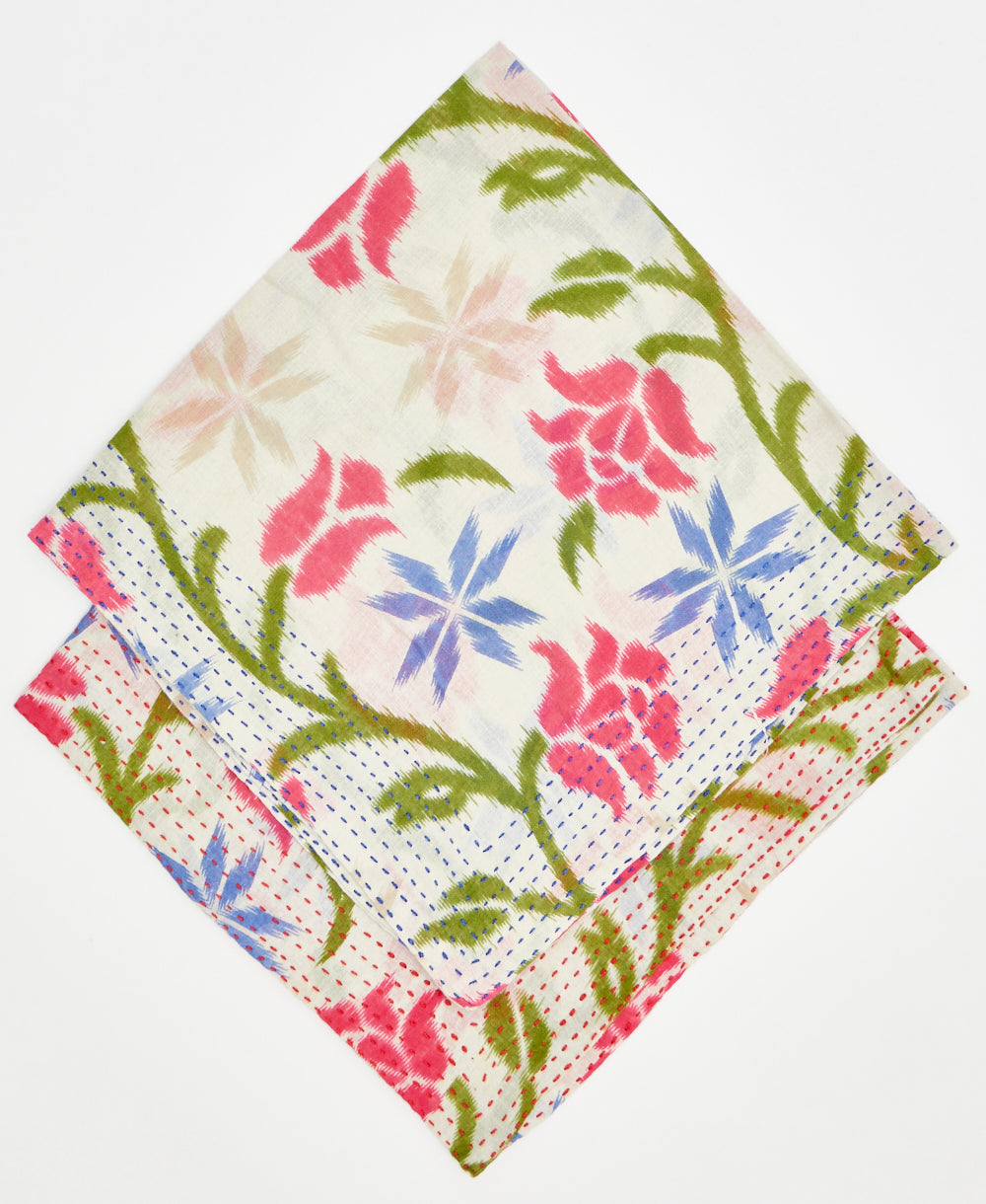 two white bandanas with red, green, and purple floral details stacked on top of each other to show their different thread colors. one has blue kantha stitching along its edges while the other has red kantha stitching 