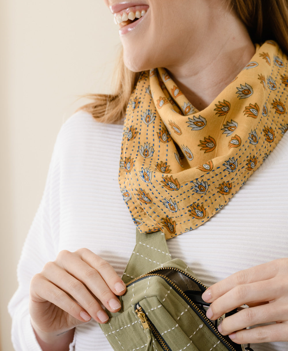 woman in a white sweater and a green bag smiling while wearing a yellow Anchal vintage cotton kantha bandana around her neck