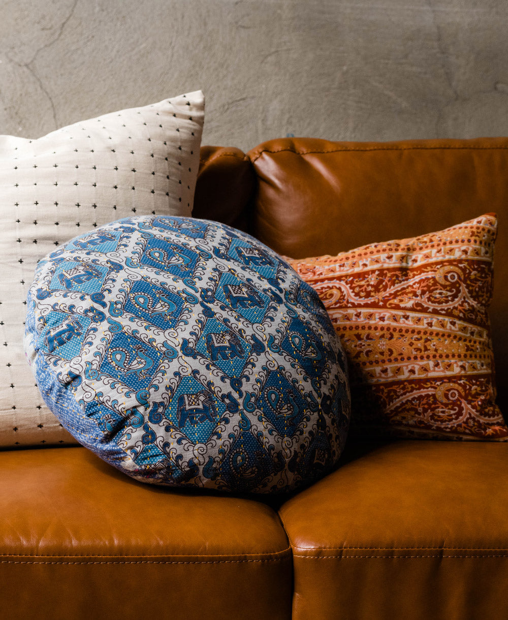 An assortment of vintage cotton pillows on a brown leather couch 