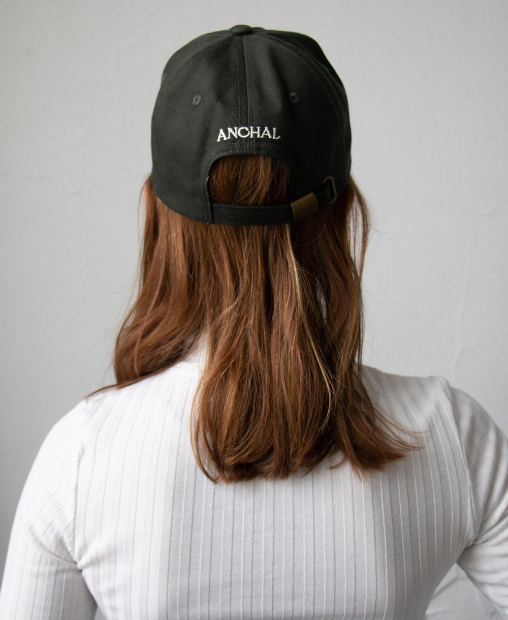 woman with red-tone mid-length hair wearing hunter green baseball cap with logo on back