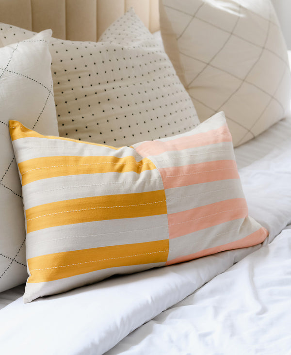 pink, yellow, and white striped lumbar pillow on a soft white bed