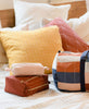 Anchal modern travel accessories sitting on a colorful bed with pillows by Anchal Project