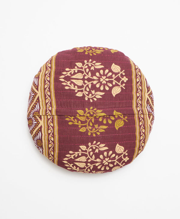 Opposite side of the pillow featuring an intricate green and cream pattern on a plum background 