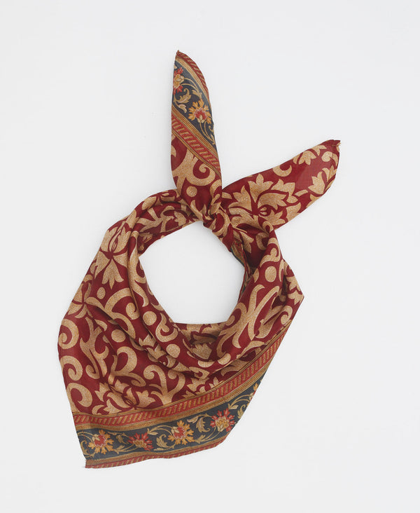 dark red silk bandana with tan swirls and a black floral border along the edge of the scarf