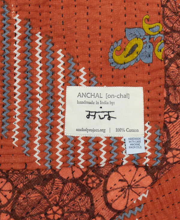 Burnt orange colored small cotton throw blanket that has multiple prints stitched together 
