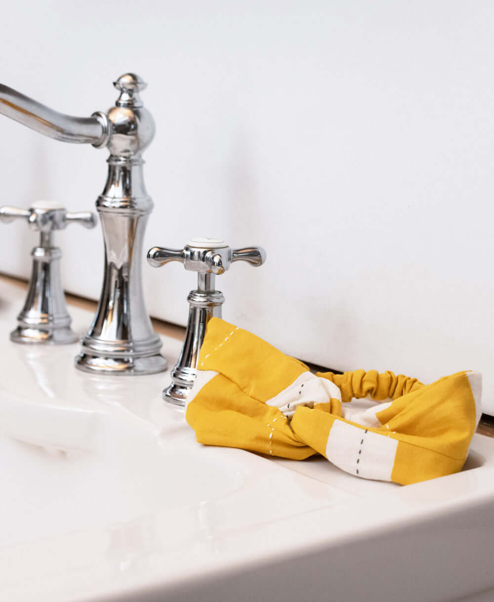 mustard yellow stripe twist headband sitting on sink vanity in modern white bathroom