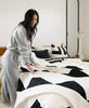 woman in gray sweatsuit making bed with geometric triangle black and white quilt by Anchal Project