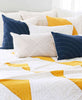 Fair trade certified bedding styled with mustard and navy pillows and throws that have been hand stitched by anchal artisans